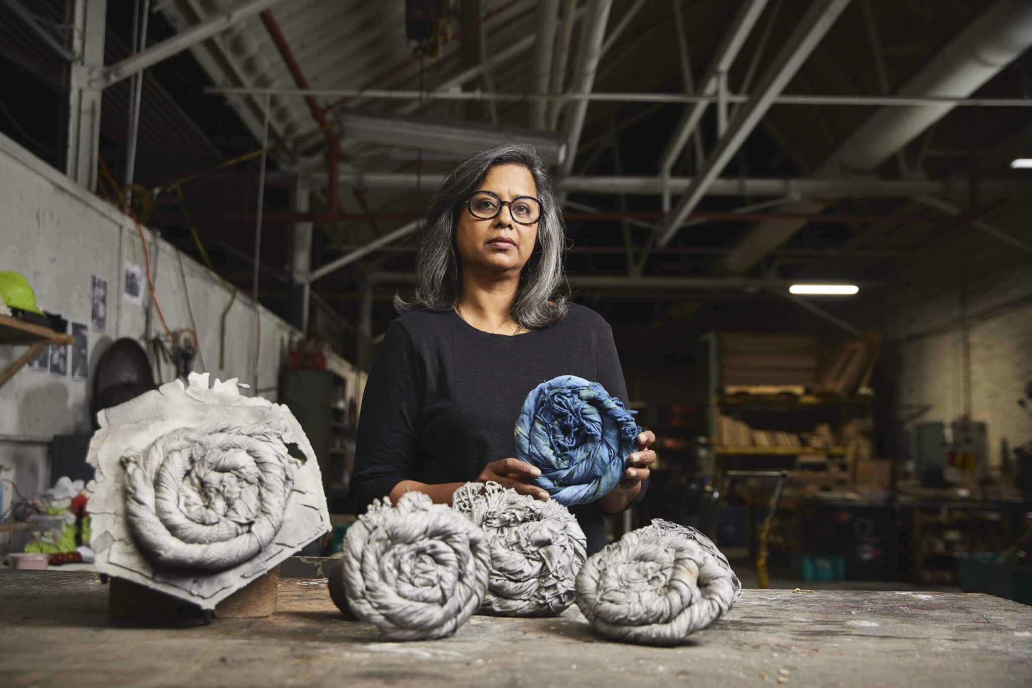 An artist holds up artwork made of coiled fabric.
